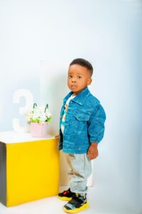 Cute child in denim jacket posing indoors beside number three decoration.